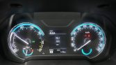 Digital car instrument cluster showing speedometer (0–180 km/h) on the right and tachometer on the left, with a central display of trip data and fuel/engine indicators.