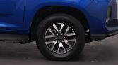 Close-up of a blue SUV's front wheel and fender, showing a silver alloy rim and tire tread visible beneath the body panel.