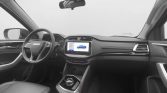 Modern car interior: driver’s seat, steering wheel, center touchscreen displaying vehicle graphics, and a rotary gear selector.