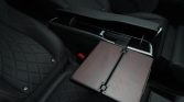 Luxurious car interior with a dark wood fold-out tray table extended between rear seats in a black leather cabin.
