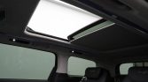 Interior of a car with a large panoramic sunroof open, black leather seats, and subtle ambient lighting.