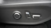 Car seat adjustment panel with a round dial and two small silver switches on a gray car interior panel.