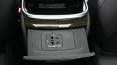 Rear center console with a 220V power outlet (150W) for passengers in a car, under wood trim accents.