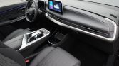 Modern car interior with a digital dashboard and center touchscreen between the front seats, almond-gray upholstery, and sleek console controls on passenger side.