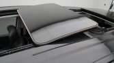 Open sunroof panel on a dark gray car roof, the glass panel retracted to reveal the opening and interior headrest.