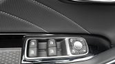 Car door interior with four window switches and a round mirror-adjustment dial set in a glossy panel, finished with stitched black leather and chrome trim.