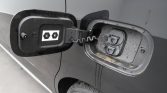 Vehicle fuel filler door open, showing the gas cap receptacle and tethered cap on a dark-colored car