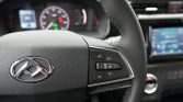 Close-up of a car steering wheel with right-side control buttons and a blurred dashboard in the background, including a visible logo center.