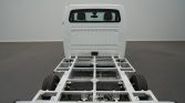 Rear view of a white truck cab on a metal chassis frame with two visible wheels, in a studio setting.