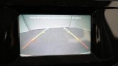 Rear parking camera view with colored guide lines (green, yellow, red) and Dutch warning text: “Houd de omgeving voor de veiligheid in de gaten!”