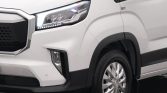 Close-up of the front left corner of a white van, showing the headlight, grille, and front wheel.