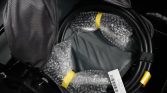 Coiled black cable with yellow end cap and bubble-wrapped sections inside a gray backpack pocket, ready for transport.