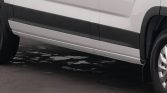Side view of a white van with black lower trim, door seams visible, and a wheel on the right; the ground shows wet patches.