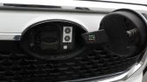 Front of a white car with the fuel filler door open and the fuel cap removed, showing the empty filler neck.