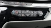 Car climate control panel: left temperature dial, central buttons for airflow and seat heaters, right knob for fan speed.