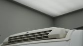 White refrigerated unit mounted on top of a truck trailer indoors, with vent grille visible on the front panel