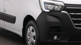 Close-up of the front left side of a white van, showing the headlight, black bumper, and front wheel.