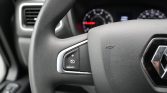 Close-up of a car steering wheel with visible Renault logo and left-side cruise control buttons, dashboard blurred in background.