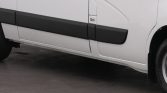 Side view of a white cargo van showing black protective side rails along the doors and a portion of the front wheel on the right side.