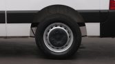 Wheel and rear section of a white van, showing a steel rim and black hubcap behind the front wheel arch