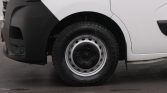 Close-up of a white van's front left wheel with a black bumper and rugged tire. Has steel rim and hubcap visible.