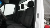 Interior of a white utility van with black fabric seats; driver’s seat at left, steering wheel visible, and a row of seats behind.