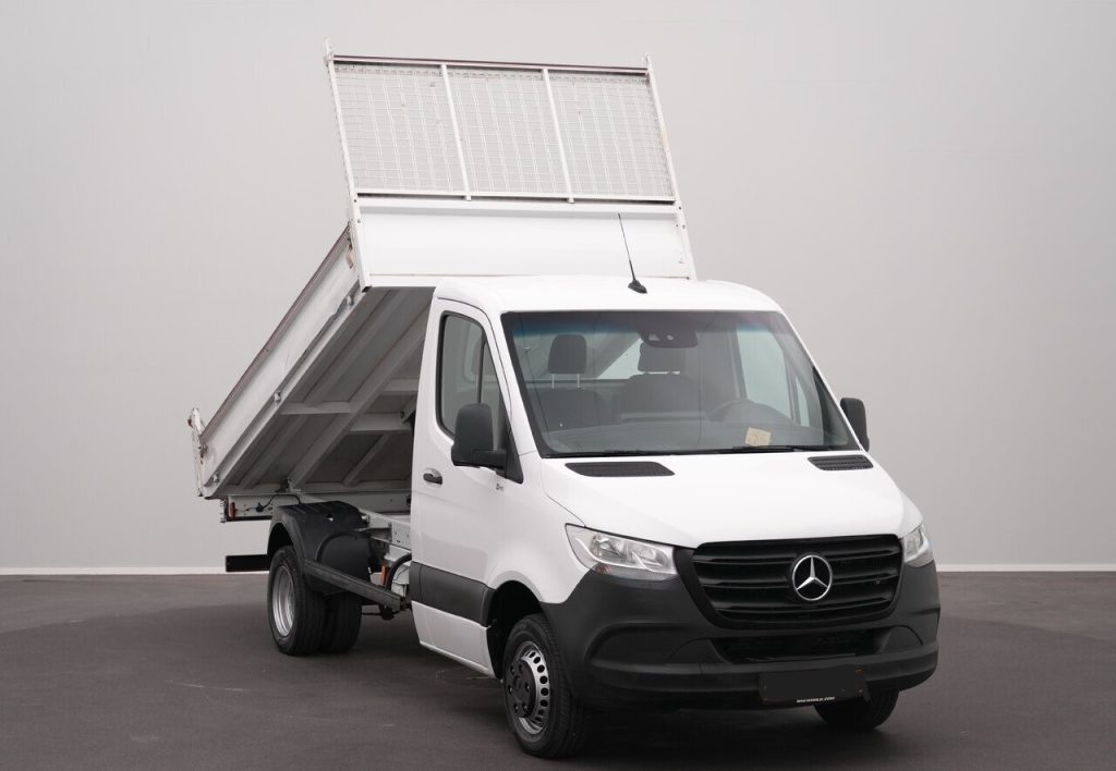 White Mercedes-Benz dump truck/van with its tilted dumping bed raised for unloading, indoors on a dark floor