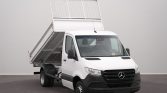 White Mercedes-Benz dump truck/van with its tilted dumping bed raised for unloading, indoors on a dark floor