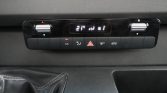 In-car climate control panel with digital display reading 21°C, two silver knobs, and a row of control buttons (A/C, defrost, hazard, rear/window defog, recirculation).