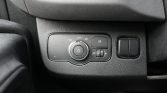 Car dashboard control panel: a circular headlight dial set to Auto with a fog light button to its right and a small vertical brightness/tilt dial, plus a blank switch further right.
