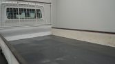 Empty pickup truck bed with a metal mesh bulkhead behind the cab window and white side panels, in a clean indoor space.