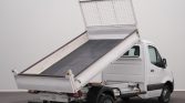 White dump truck with its cargo bed raised, ready to unload on a gray backdrop, side view of the vehicle
