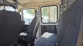 Interior of a white van showing row of gray fabric seats and a large side window; sunlit and clean interior view