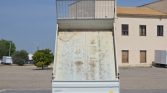 Rear view of a dump trailer with its bed raised for unloading in an industrial area on a clear day