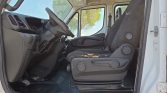 Interior of a white truck cab showing the steering wheel, dashboard, and two front seats; the passenger seat has torn upholstery and exposed filling, with a rubber floor mat below.