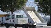 White utility truck with a hydraulic dump bed raised to unload materials in a parking lot area.