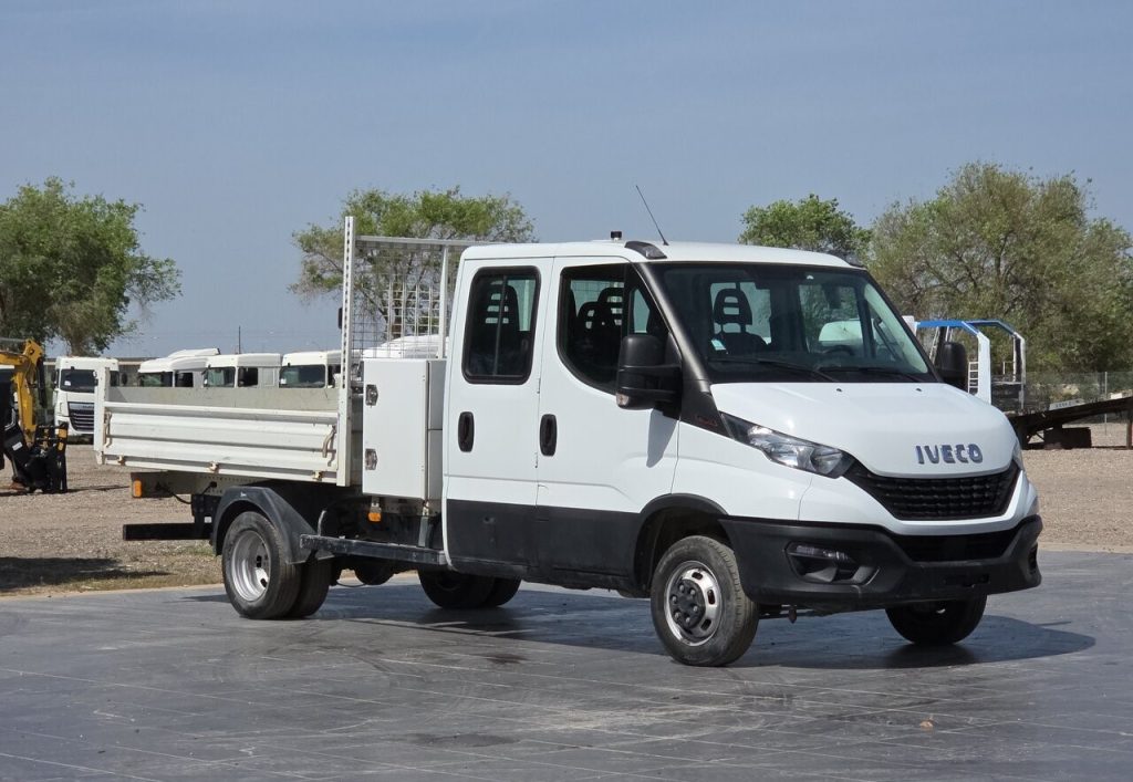 White Iveco flatbed utility truck parked in an open lot with equipment in the background