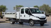 White Iveco flatbed utility truck parked in an open lot with equipment in the background