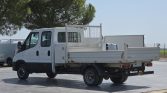 White flatbed utility truck with a metal rear cage, parked in an outdoor lot on a sunny day