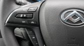 Close-up of a car steering wheel showing cruise-control buttons on the left and a blurred dashboard in the background.