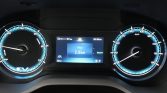 Car instrument cluster with blue-lit gauges; center digital display shows Trip1 1.6 km and status icons on both sides (EV badge visible).