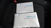 Two Maxus eDELIVER 9 manuals in plastic sleeves resting on a black car seat.
