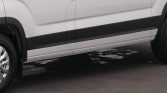 Side view of a white van with a black lower body molding, wheel visible, parked on dark pavement with small snow patches nearby