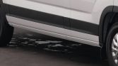 Side view of a white van with black side trim, showing the rear wheel on the right and a small puddle beneath on the pavement.