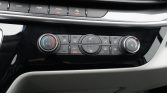 Center console climate control panel in a car: left temperature dial with blue and red A/C markings, middle row of buttons for airflow and heated seats, and right dial for fan speed with a red indicator