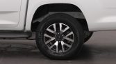 Close-up of a silver alloy wheel and tire on a white vehicle, showing the wheel well and road surface beneath.