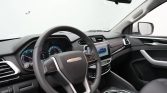 Modern car interior with steering wheel, digital gauges, center touchscreen displaying a blue car, and a rotary gear selector.