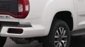 White pickup truck rear quarter with visible taillight, bumper, and alloy wheel; EV badge on tailgate edge.