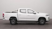 Side view of a white double-cab pickup truck in a studio setting, showing bed, rails, and alloy wheels