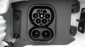 Close-up of an electric vehicle charging inlet showing a round 7-pin connector above and two larger pins below.